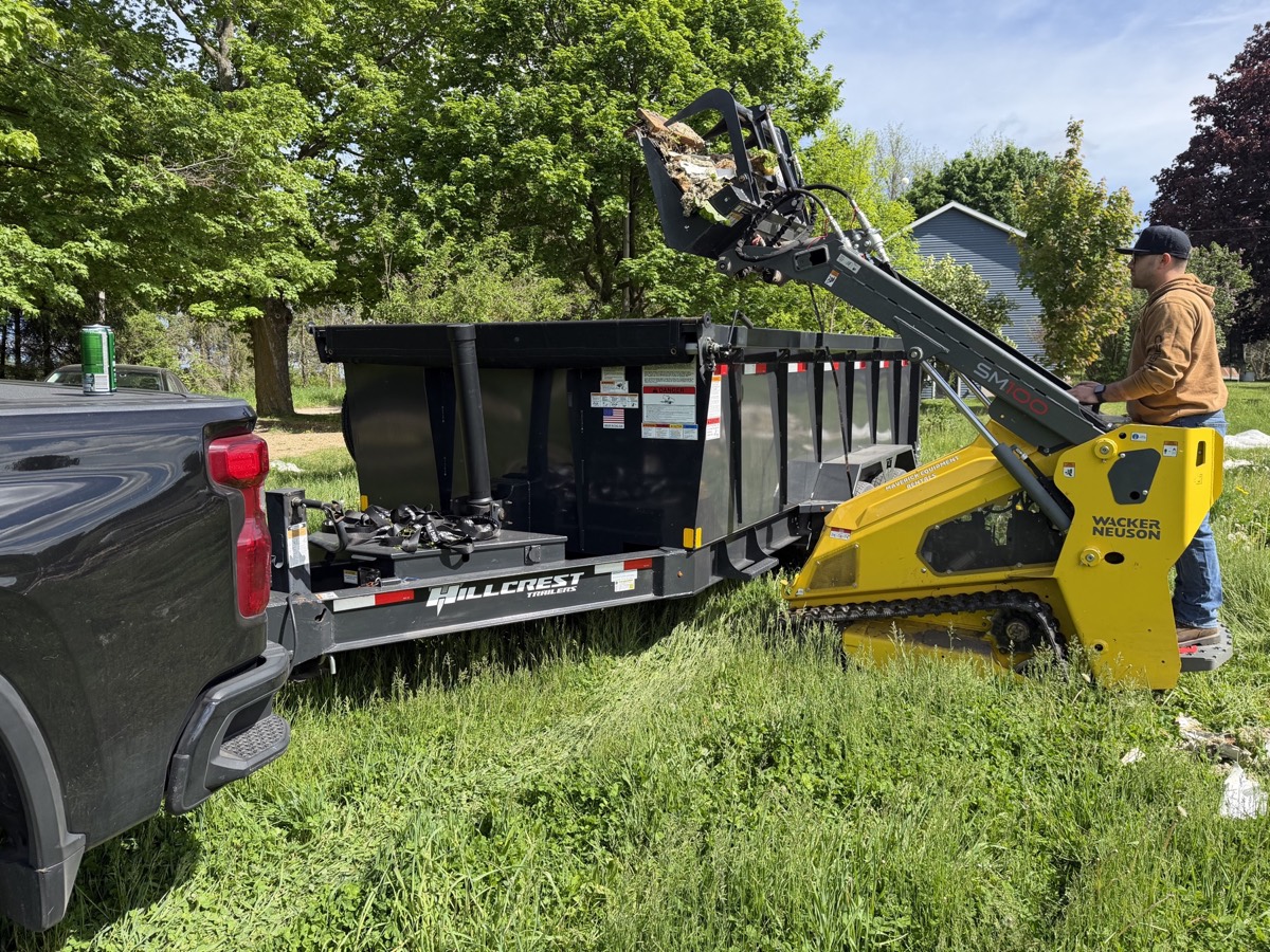 Skid-steer loading debris into a Haul-It Heroes trailer
